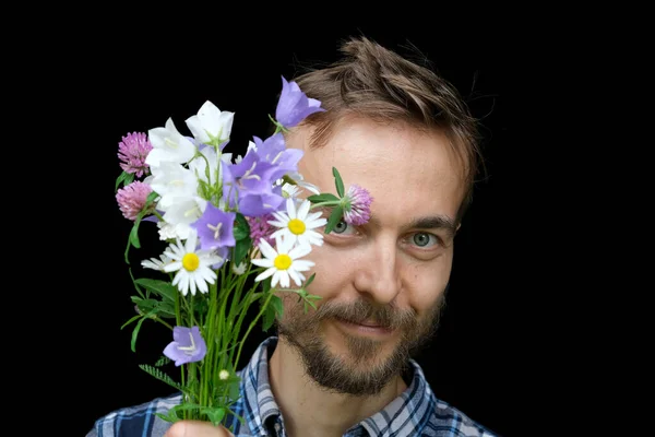 Handsome bearded stylish man with bouquet of tender wild flowers on black background. Greeting card, pastoral spring or summer mood banner.