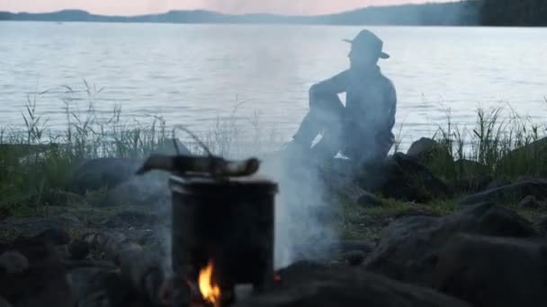 페도라 모자를 관광객은 저녁에 호숫가에 앞마당에 모닥불 위에서 끓는다 하이킹 — 비디오