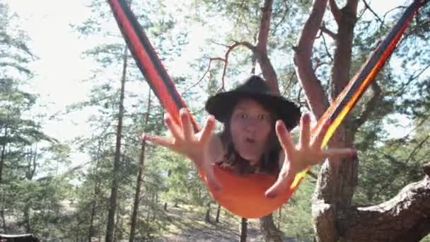 穿着毛毡帽子的有趣的女游客在松树林中的吊床上摇曳着 试图用手去拿相机 快乐的微笑着的女徒步旅行者放松于大自然 积极的户外生活方式 — 图库视频影像