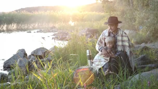 日落时 当地旅客的父亲和儿子坐在湖边 爸爸用毛毯把孩子包起来 以表友善 与家人共度时光 — 图库视频影像