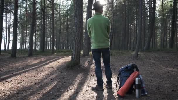 日落时分 站在松树林中 戴着带背包和锯齿状装备的毛毡帽的登山冒险家男子 当地旅行 — 图库视频影像