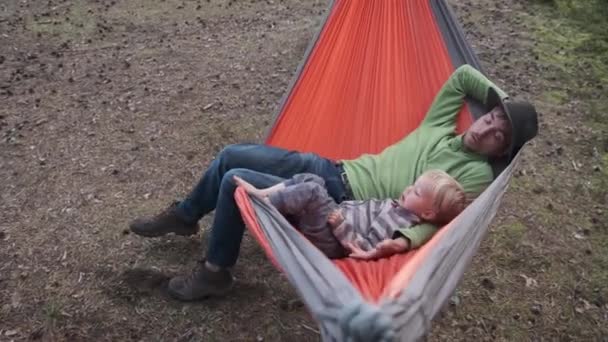父子俩徒步旅行者坐在森林里的旅游吊床上 积极参加家庭户外活动 旅行和与孩子一起探险 侧视图 — 图库视频影像