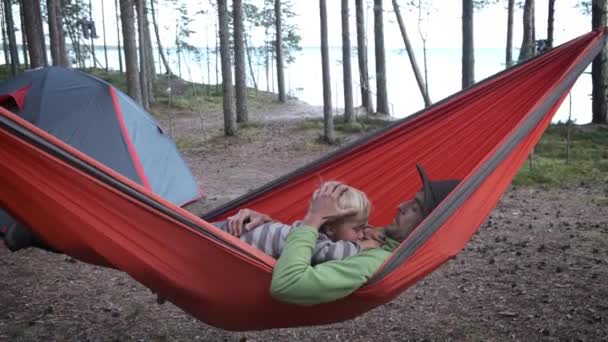 积极参加家庭户外活动 旅行和与孩子一起探险 父亲和儿子徒步旅行者坐在森林露营帐篷附近的旅游吊床上 — 图库视频影像