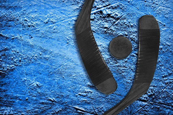 Dwa Kije hokejowe i krążek na niebieskim lodzie — Zdjęcie stockowe