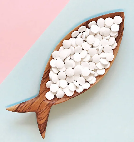 Calcium pills in a wooden dish in the form of a fish. Fish is rich in calcium. Color background. Flay lay, top view. Space for text Royalty Free Stock Photos