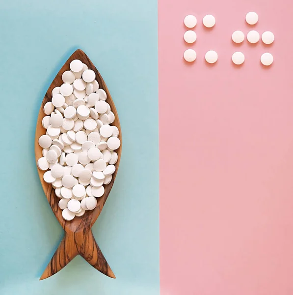 Calcium pills in a wooden dish in the form of a fish. Fish is rich in calcium. Color background. Word of CA (calcium) is laid out by pills. Flay lay, top view Stock Image