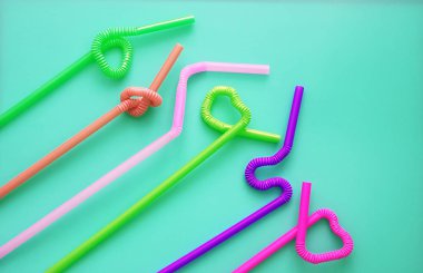 Mavi bir arka plan üzerinde düğüm veya zikzak veya kalp şeklinde bükülebilen esnek bir parçaya sahip renkli plastik kokteyl tüpleri. Modern ve modaya uygun renkler. Eko kavramı