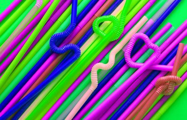 Esnek bir parçaya sahip renkli plastik kokteyl tüpleri, yeşil bir arka plan üzerinde düğüm veya zikzak veya kalp şeklinde bükülebilir. Modern ve neon moda renkler. Eko kavramı