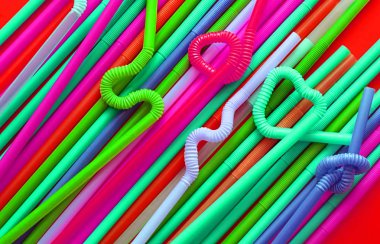 Kırmızı bir arka plan üzerinde düğüm veya zikzak veya kalp şeklinde bükülebilen esnek bir parçaya sahip renkli plastik kokteyl tüpleri. Modern ve neon moda renkler. Eko kavramı