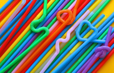 Esnek bir parçaya sahip renkli plastik kokteyl tüpleri, sarı bir arka plan üzerinde düğüm veya zikzak veya kalp şeklinde bükülebilir. Eko kavramı