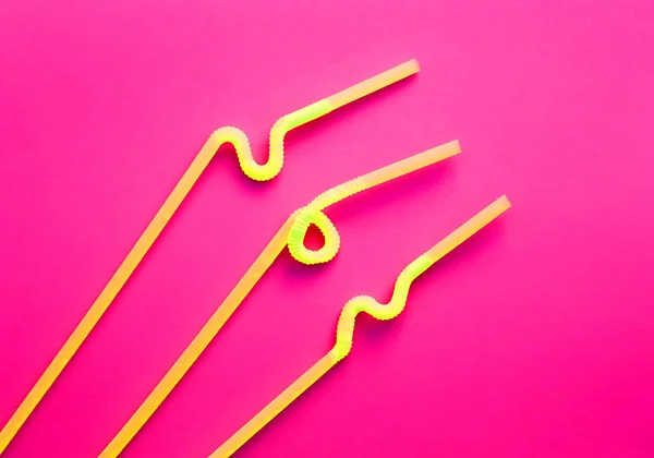 Gelbe Plastikcocktailröhrchen mit einem flexiblen Teil, aufgrund dessen sie zu einem Knoten oder einem Zickzack auf karminrotem Hintergrund verdreht werden können. moderne und trendige Farben. Öko-Konzept — Stockfoto