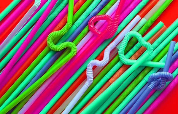 Цветные пластиковые коктейльные трубки с гибкой частью, благодаря чему они могут быть скручены в узел или зигзагом, или в форму сердца, на красном фоне. Современные и неоновые модные цвета. Эко-концепция — стоковое фото