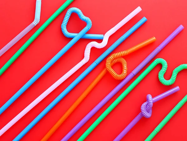 Цветные пластиковые коктейльные трубки с гибкой частью, благодаря чему они могут быть скручены в узел или зигзагом, или в форму сердца, на красном фоне. Современные и модные цвета. Эко-концепция — стоковое фото