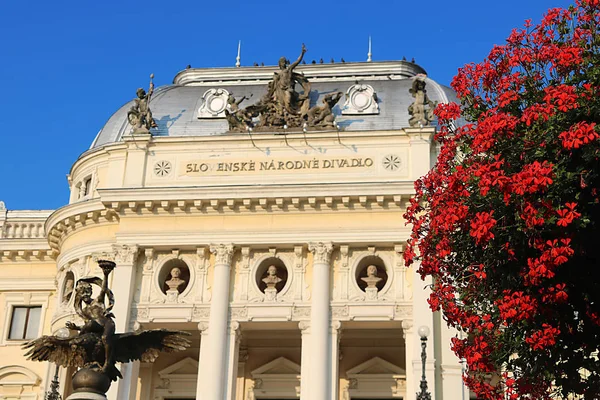 Pohled shora na Slovenské národní divadlo a červené květy v Bratislavě, Slovensko. Novorenesanční budova byla postavena v roce1886. Selektivní zaměření na červené květy — Stock fotografie