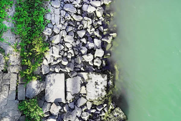 Blick von oben auf das felsige Ufer des Flusses und Wasser, grüne Pflanzen. Wasserkante und große Felsbrocken. Kopierraum — Stockfoto