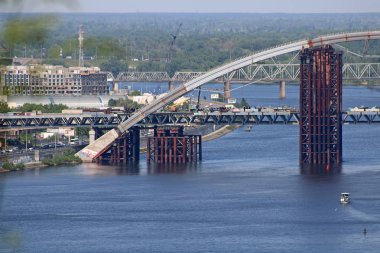 Kyiv, Ukrayna - 18 Mayıs 2019: Dinyeper Nehri üzerinde Podilsko-Voskresensky Köprüsü inşaatı. Sol tarafta ağaç yaprakları.