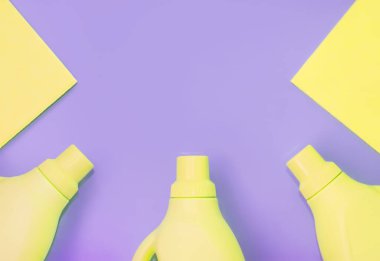 Temizlik için kimyasallar, temizlik için paçavralar içeren sarı plastik şişeler. Mor arka plan. Temizlik kavramı