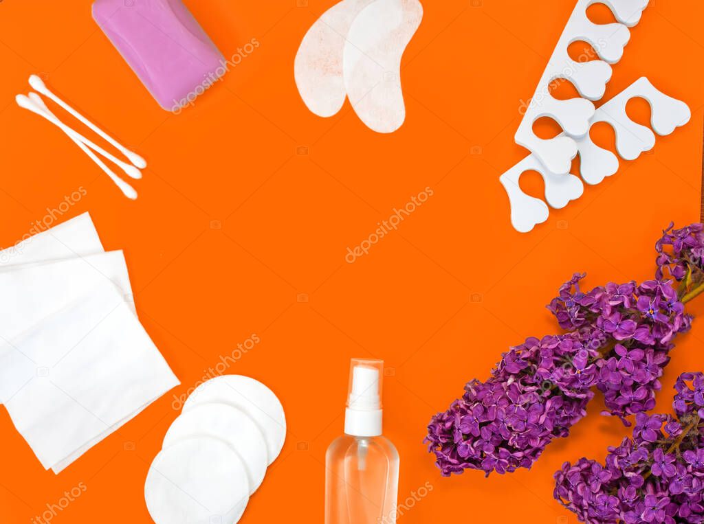 Hygiene products and lilac flowers laid out as a frame. Soap, patches, sanitizer, wet wipes, ear sticks, cotton pads and pedicure separators. Personal Care Concept. Orange background