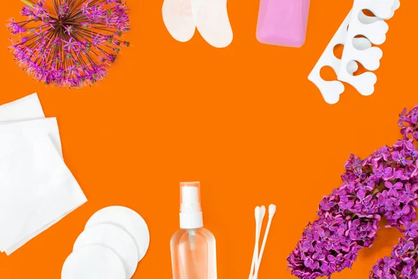 Hygiene products, lilac flowers and garlic flower laid out as a frame. Soap, patches, sanitizer, wet wipes, ear sticks, cotton pads and pedicure separators. Personal care Concept. Dark orange background.