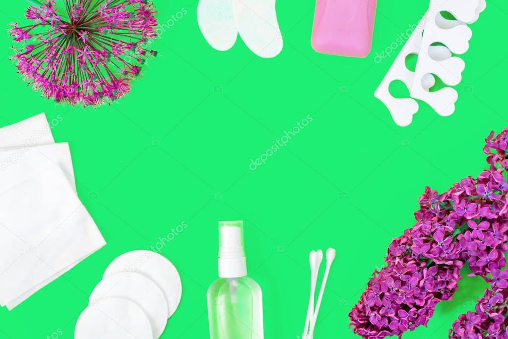 Hygiene products, lilac flowers and garlic flower laid out as a frame. Soap, patches, sanitizer, wet wipes, ear sticks, cotton pads and pedicure separators. Personal care Concept. Green background.