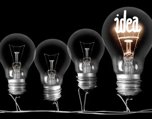 Photo of dark and shining light bulbs with fibe in IDEA shape; concept of idea, innovation, uniqueness and standing out; isolated on black background