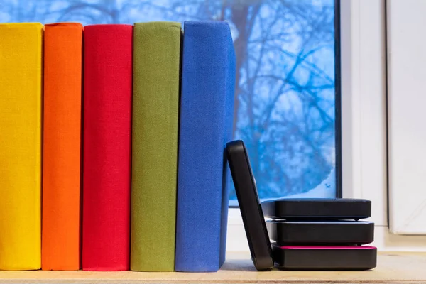 New and traditional. External hard drive on the multi-colored books near the window