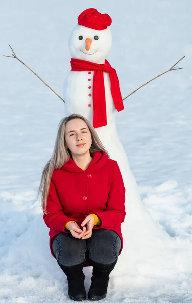 魅力的な女性で赤コートで座って近く雪だるま — ストック写真