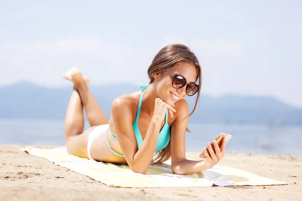 性感的女孩与太阳镜和智能手机日光浴在海滩上 — 图库照片