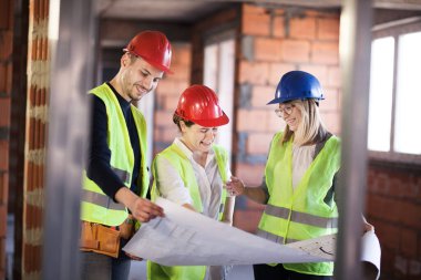 Yelekli ve kasklı mühendislerden oluşan bir ekip bir inşaat sahasının şemalarıyla.