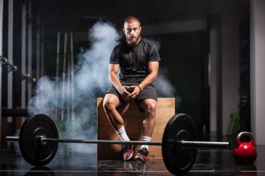 Halter ekipmanlı kaslı bir sporcu. Spor salonunda Crossfit antrenör. Duman arkaplanı.