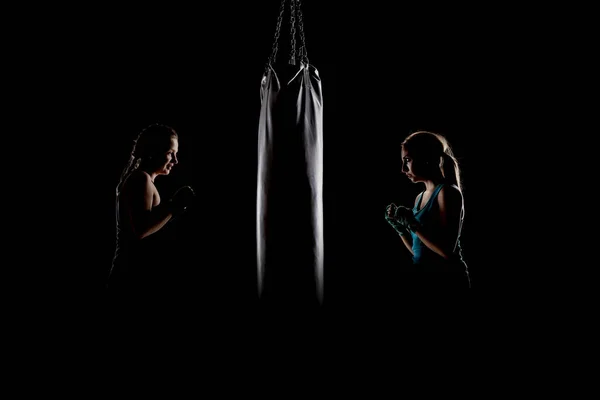 ボクシングバッグの横に立つ2人のキックファイターの女の子 — ストック写真