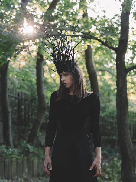 Witch woman with crown standing in forest