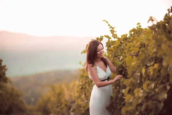 Mujer sonriente en vestido blanco de pie en el viñedo —  Fotos de Stock