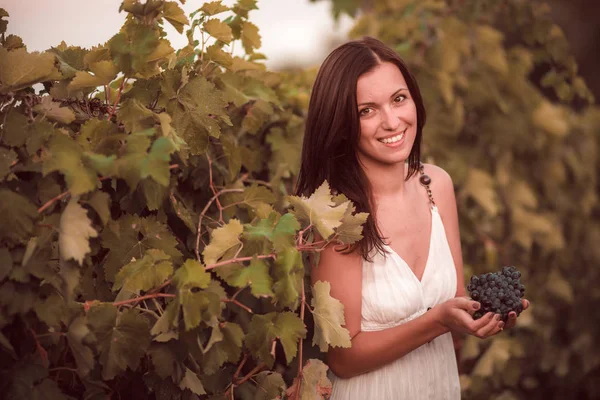 Mujer sonriente en vestido blanco de pie en el viñedo — Foto de Stock