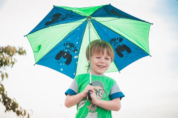 Garçon souriant tenant un parapluie sous la pluie et le soleil — Photo