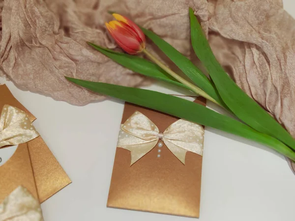 Pozdrav karty ležící na bílém stole s tulipánem a jemnou růžovou šálou. — Stock fotografie