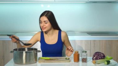 Genç bir kadın çorba pişiriyor ve onu tadıyor.