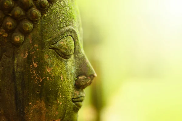 Buddha head worn out. Outdoors in Thailand, Laos, Myanmar, Cambodia, India, Sri Lanka, with green moss growing in the rainy season.