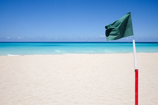 Green flag on a sandy beach against the ocean — Stock Photo, Image