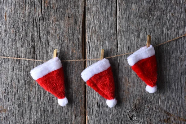 三个圣诞老人的帽子悬挂在一条缠绕在乡间木墙上的绳子上 — 图库照片