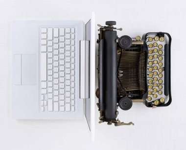 Top view of a white desk with old fashioned typewriter back-to-back with a modern laptop computer.