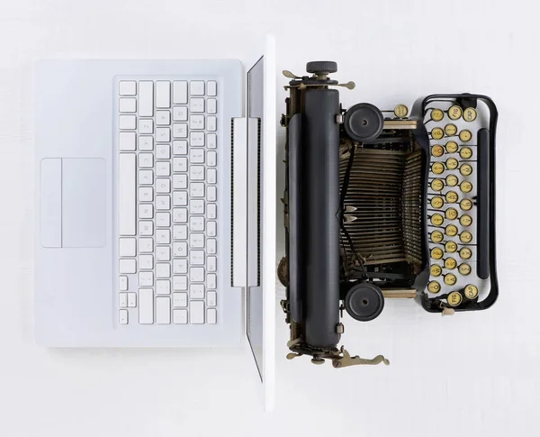 Top view of a white desk with old fashioned typewriter back-to-back with a modern laptop computer.