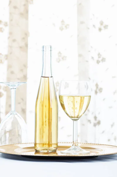 Bottiglia di vino bianco e bicchiere su un piatto d'oro davanti a un vento — Foto Stock
