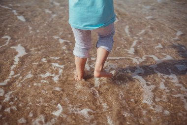 Tropik sahilde kum üzerinde çocuğun bacakları.