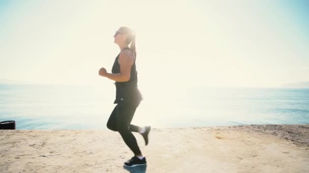 日の出の海辺に走っている女性 午前中にスポーツを行う強いアスリート — ストック動画
