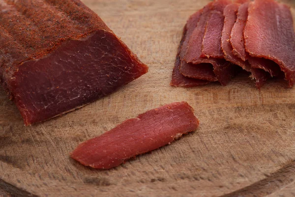 Basturma, lomo seco de carne de res, cortado en rodajas finas, sobre una tabla de madera plana, aislado sobre fondo blanco . — Foto de Stock