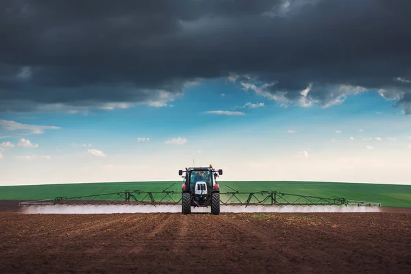 Landbouwtrekker ploegen en sproeien op het veld — Stockfoto