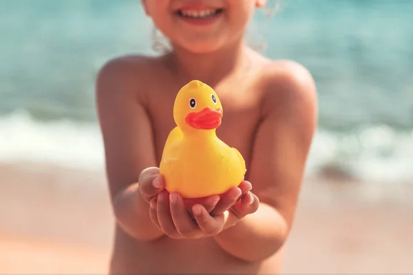 Маленькая девочка держит в руках жёлтую резиновую утку на пляже — стоковое фото