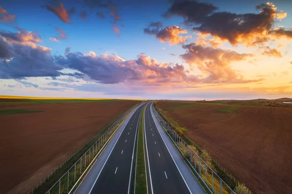 Flygfoto över motorvägen vid solnedgången. Transportbakgrund. Landskap med väg nära åkrar. — Stockfoto