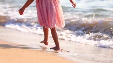 Güzel okyanus sahilinde gün doğumunda yürüyen küçük bir kız. Mutlu yaz tatili. 